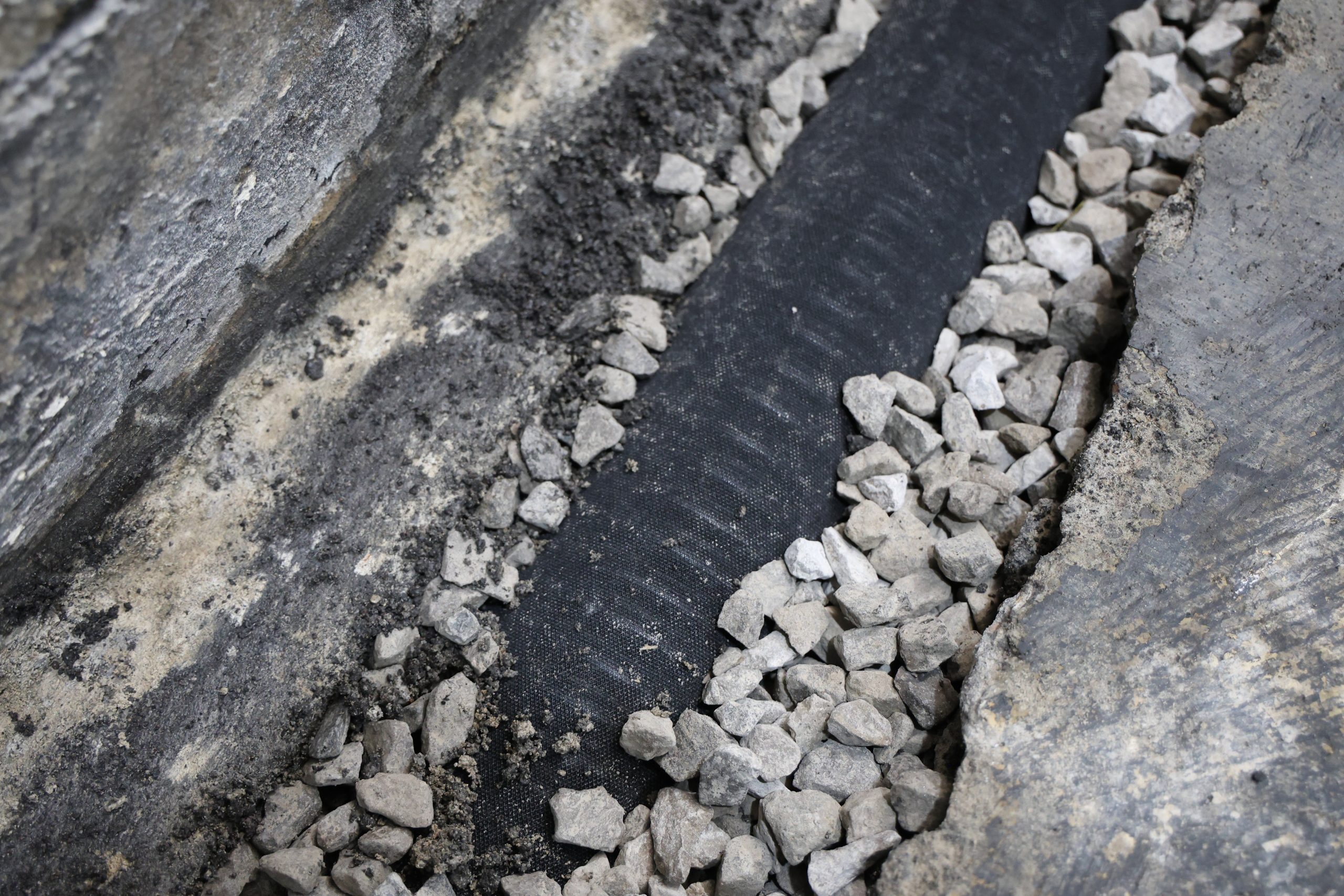 Exterior gravel drainage trench along a concrete foundation wall