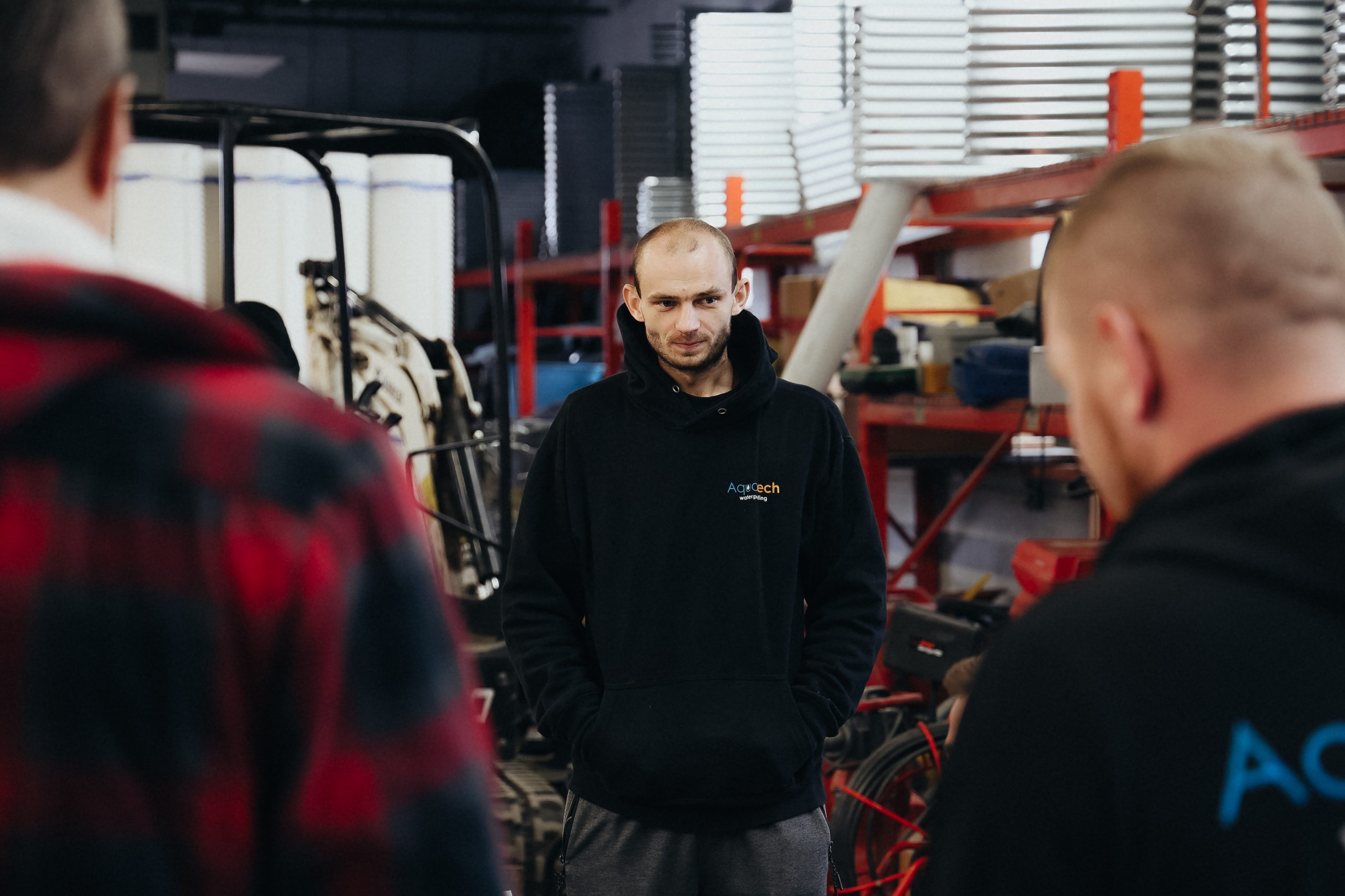 Aquatech Waterproofing staff member standing in a warehouse workshop environment with other team members