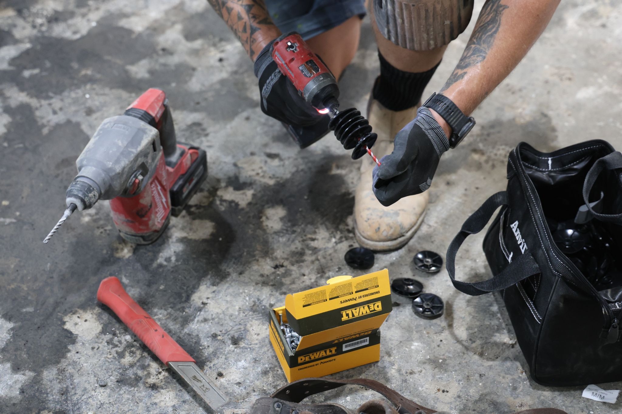 Aquatech Waterproofing technician preparing drill, fasteners, and tools on concrete floor