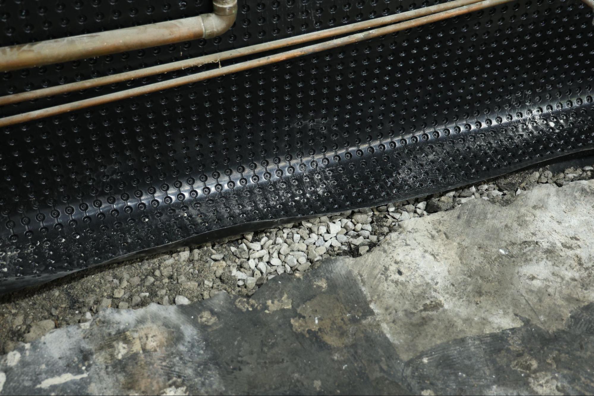 Close-up of black dimpled waterproofing membrane edge installed along basement wall above gravel drain