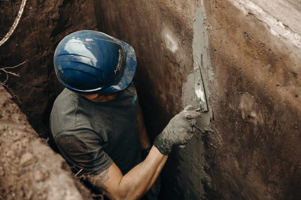 Aquatech Waterproofing technician applying hydraulic cement to repair foundation wall crack in trench