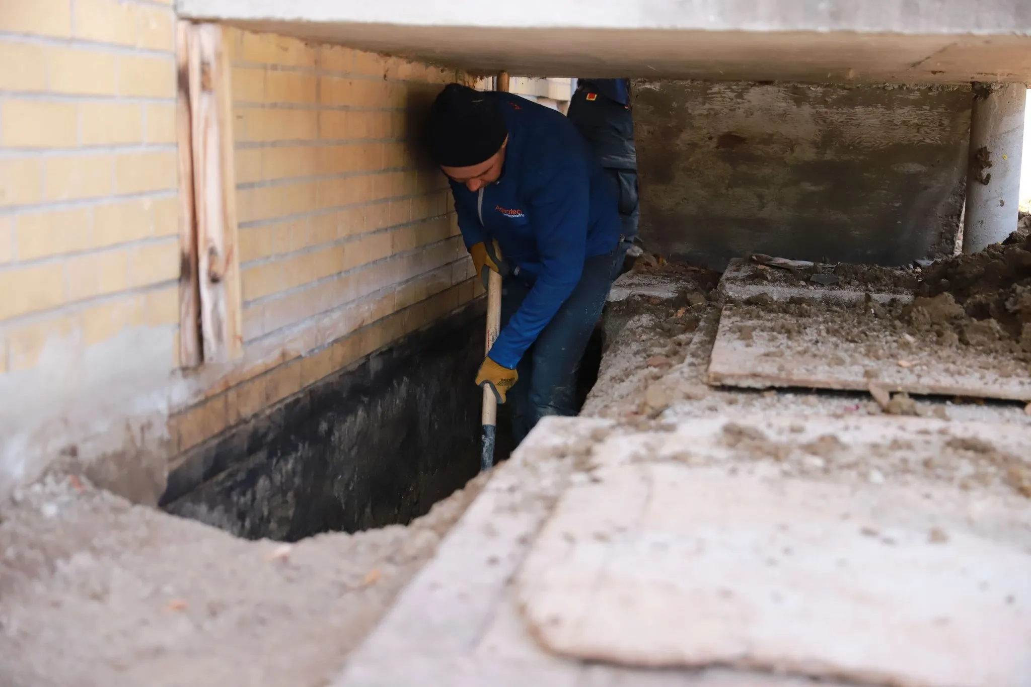 Aquatech waterproofing technician working on basement foundation wall