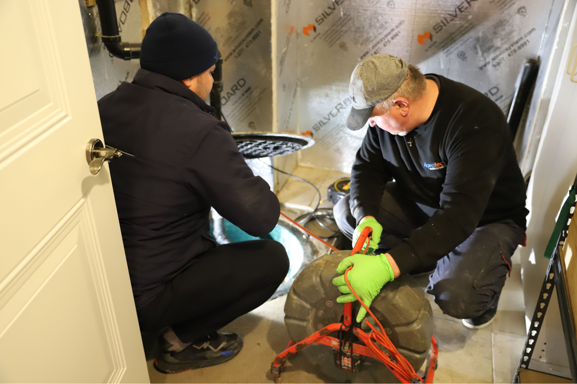 Aquatech technicians installing backwater valve in Toronto basement using power tools
